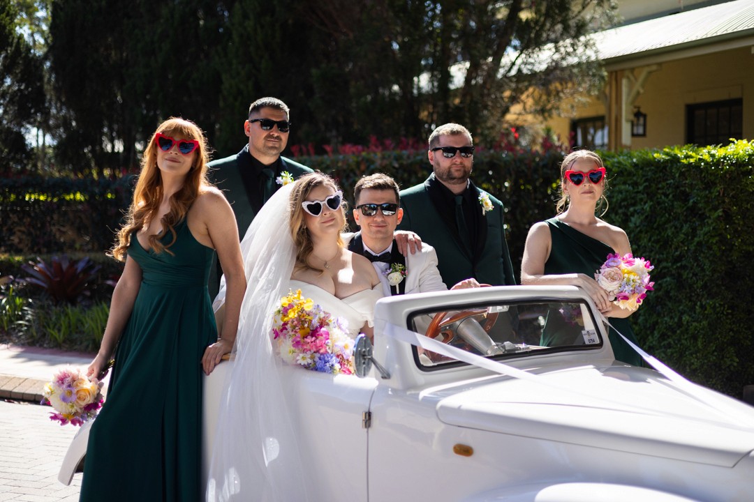 Bride and groom in old fashioined car surounding by bridal party
