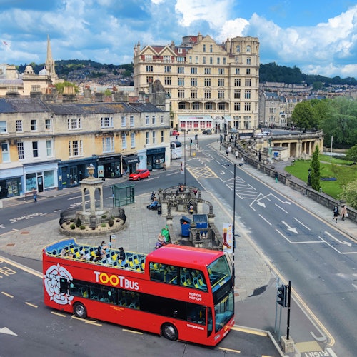 一辆红色双层Tootbus巴士穿过一座历史悠久的城市,城市里有高大的建筑物、街道交叉口,还有行人走动。