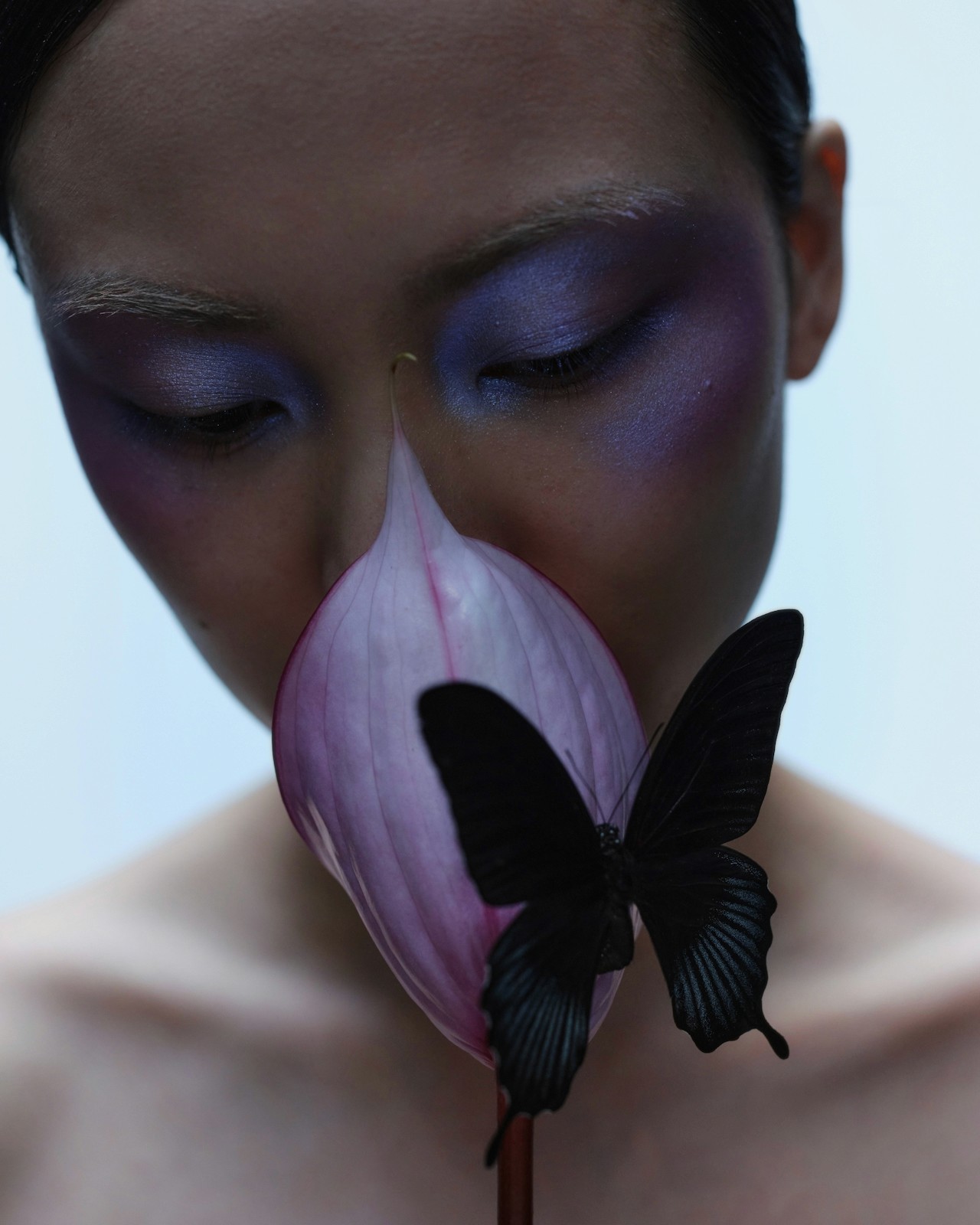 A woman gently smelling a flower with a butterfly perched on it.