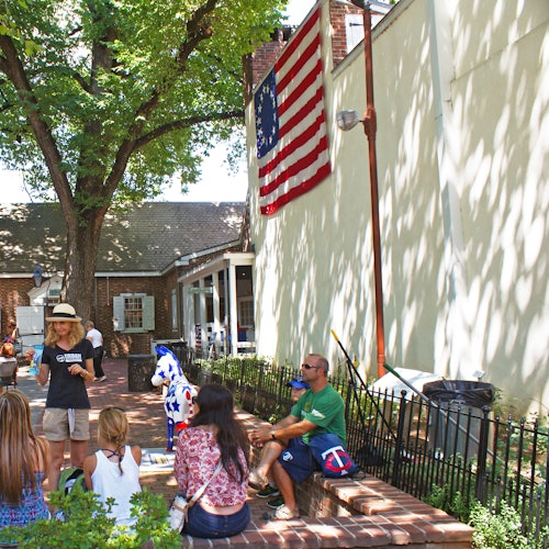 一群人坐着和站在一座砖砌建筑和美国国旗旁的阴凉庭院里。