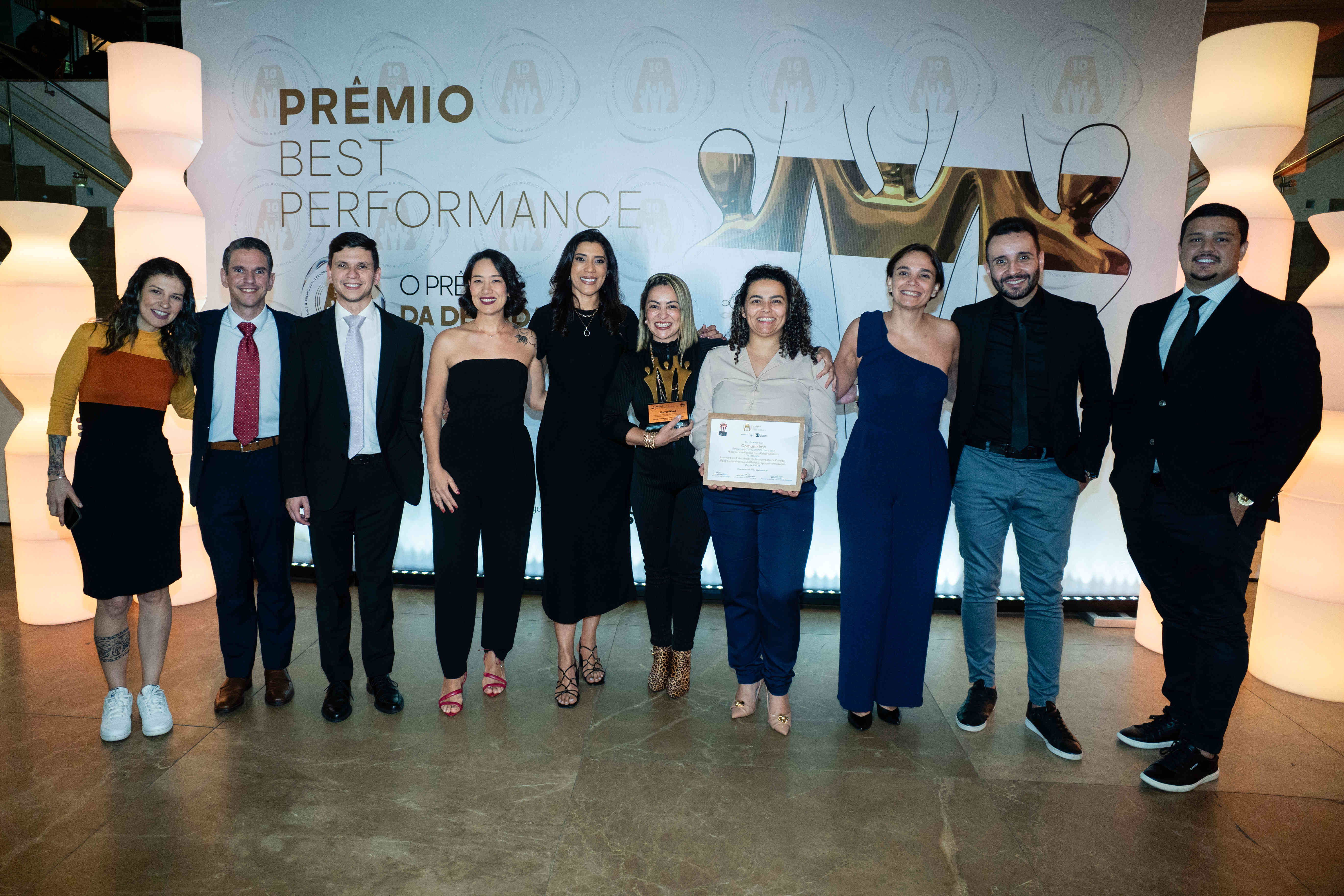 Executivos da Comunikime posando com troféu bronze e certificado no palco do Prêmio Best Performance 2025