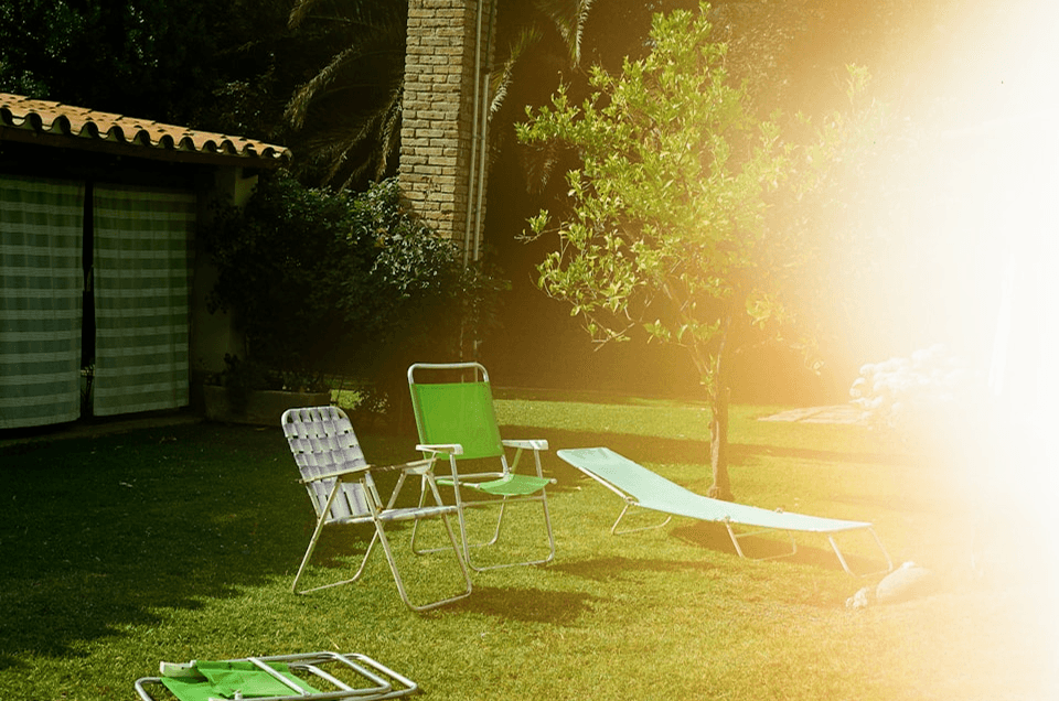 Sunlit garden with empty lounge chairs on green grass beside a house — symbolizing calm presence, consistent visibility, and how LinkedIn ghostwriting helps B2B leaders stay top of mind without constant manual effort.