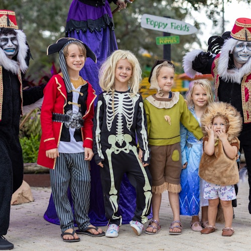 Children dressed in various costumes, including a pirate, skeleton, and lion, posing with two people in gorilla suits.
