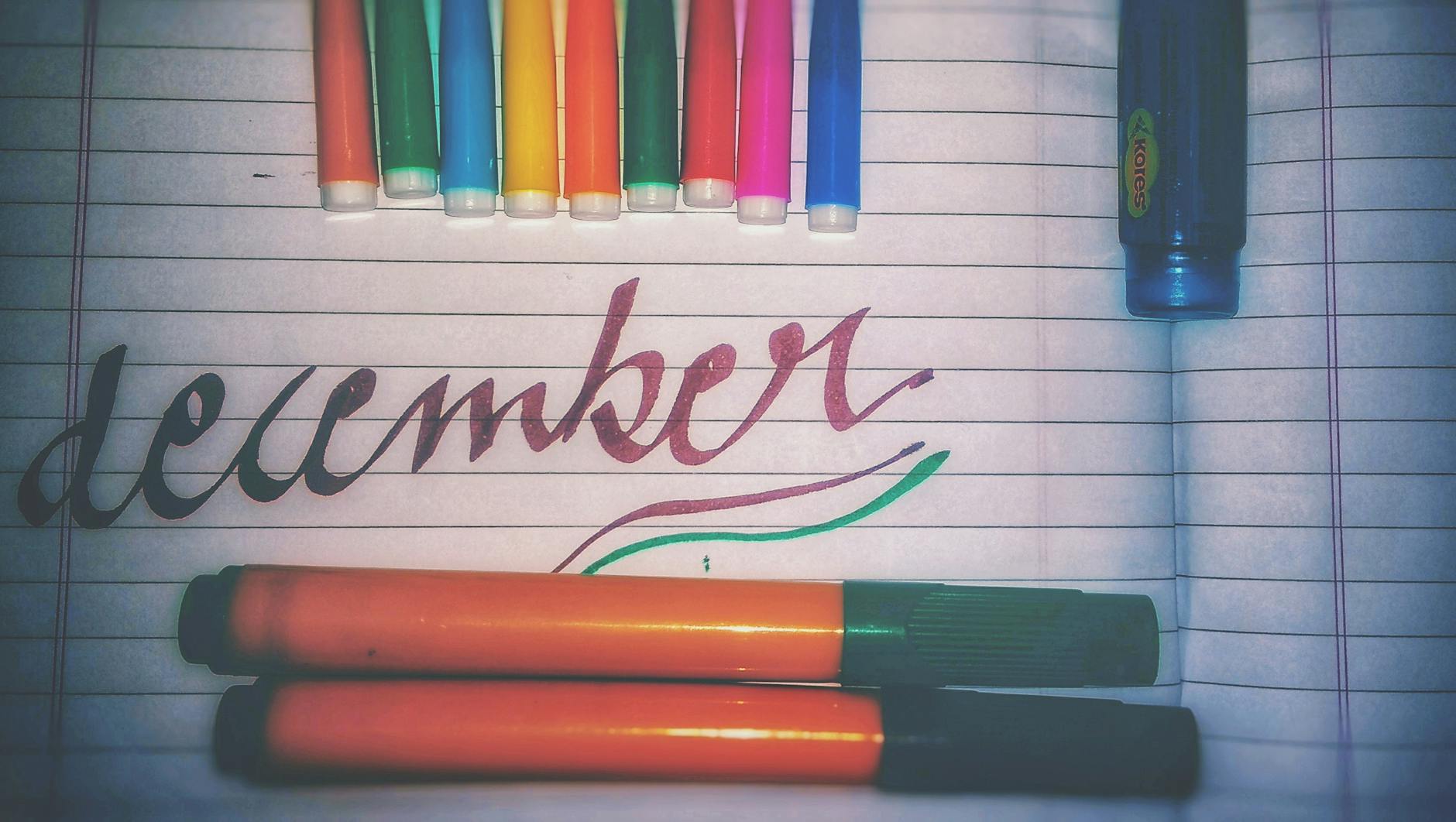 A smiling teacher sits at a wooden desk using colorful markers and washi tape to customize her academic organizer.