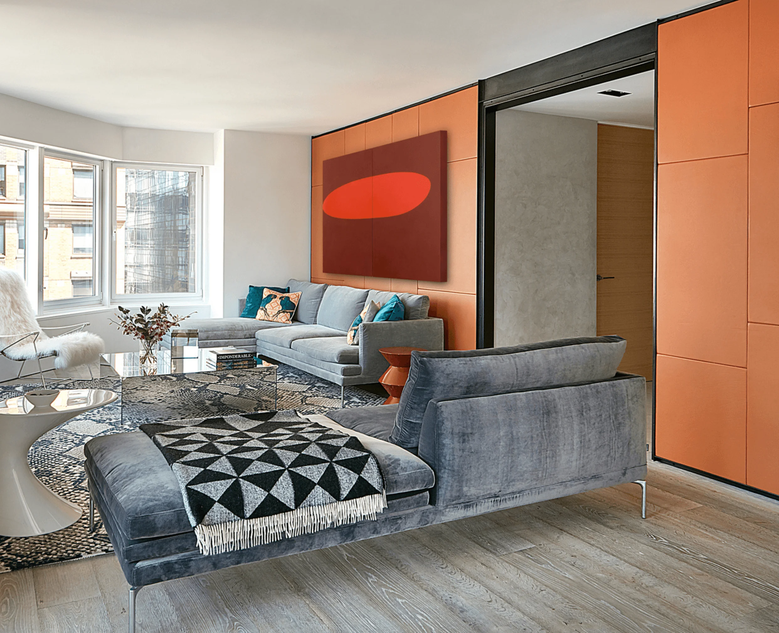 The living room at CitySpire Duplex, with a gray velvet sectional beneath a red abstract painting and rust-colored leather wall panels