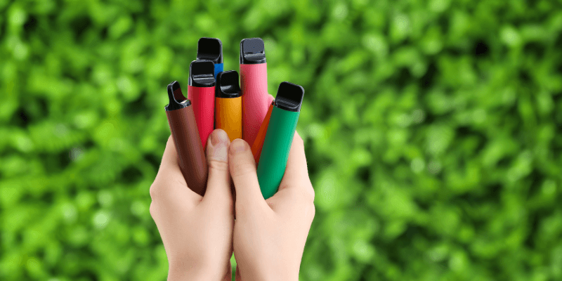 Seseorang memegang beberapa vape pelbagai warna di tangan.