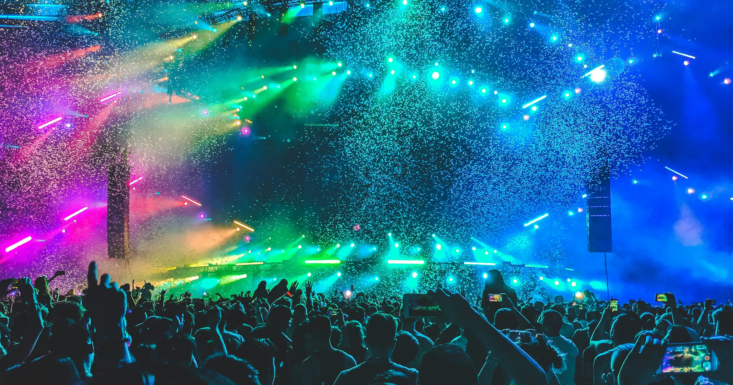 Crowd at a music festival enjoying a vibrant light show with confetti in the air.