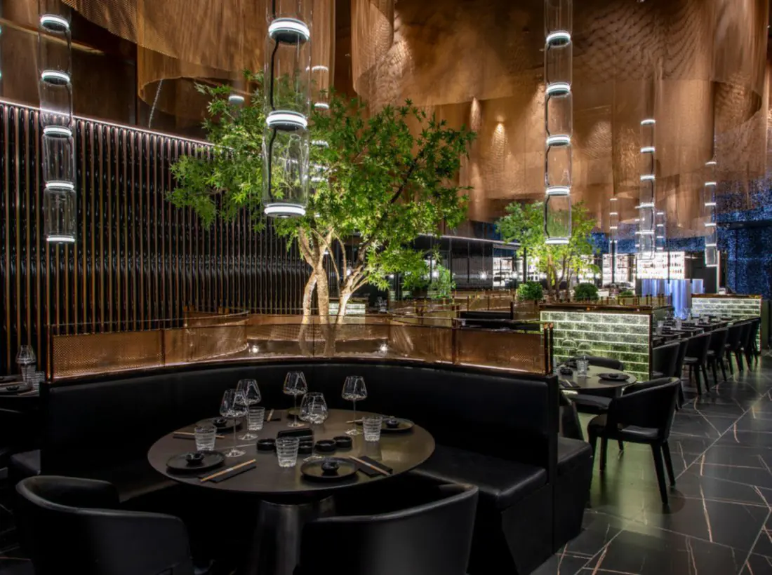 Table ronde sur banquette noire, arbres éclairés et colonnes de verre à anneaux lumineux