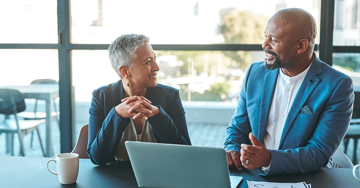 Woman in glasses interviews man at office desk.