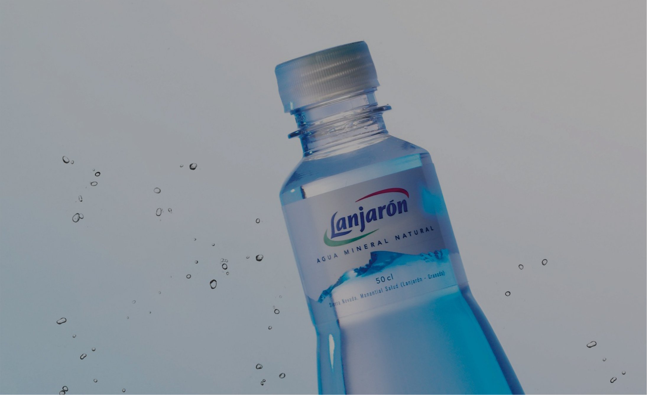Clear plastic bottle of Lanjarón mineral water on a light background, angled with droplets around it. The image conveys freshness and purity.
