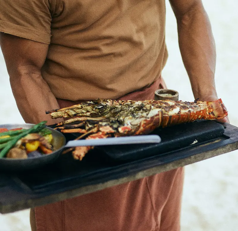 Maresias restaurant at Be Tulum: grilled lobster dish served by a man to a diner, accompanied by vegetables.