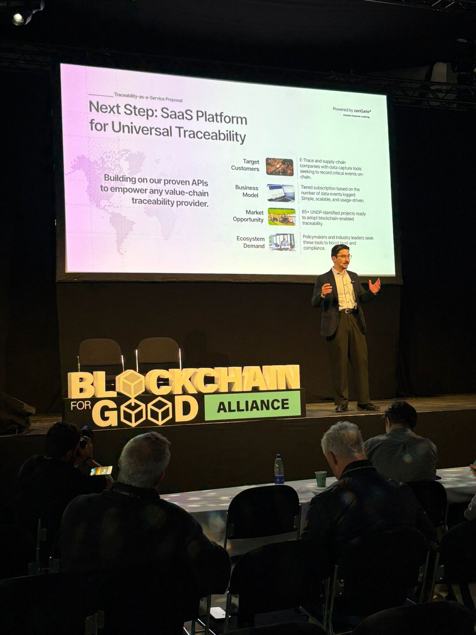 Man with tousled hair sitting at a cluttered desk in a dimly lit room. Warm, orange lighting creates a moody and contemplative atmosphere.