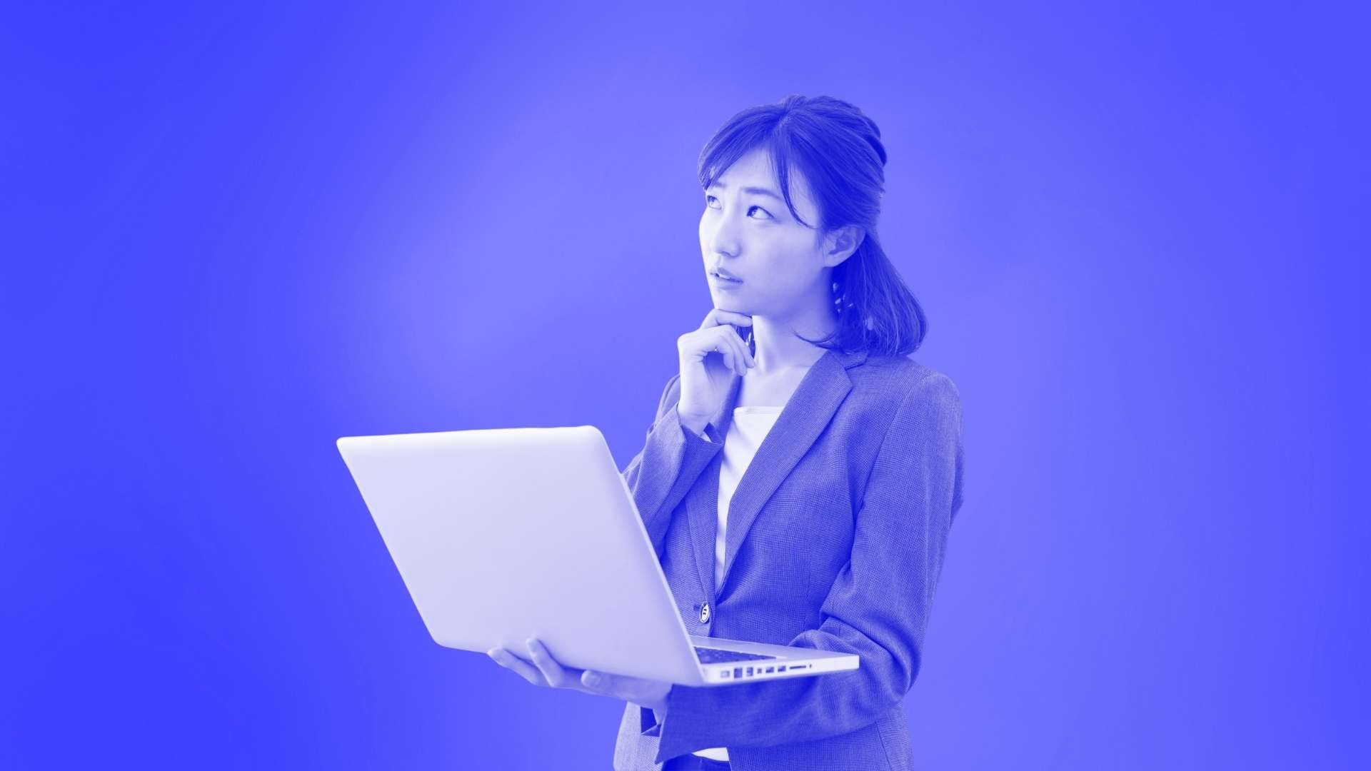 A woman wearing a suit jacket holding her laptop and looking pensive