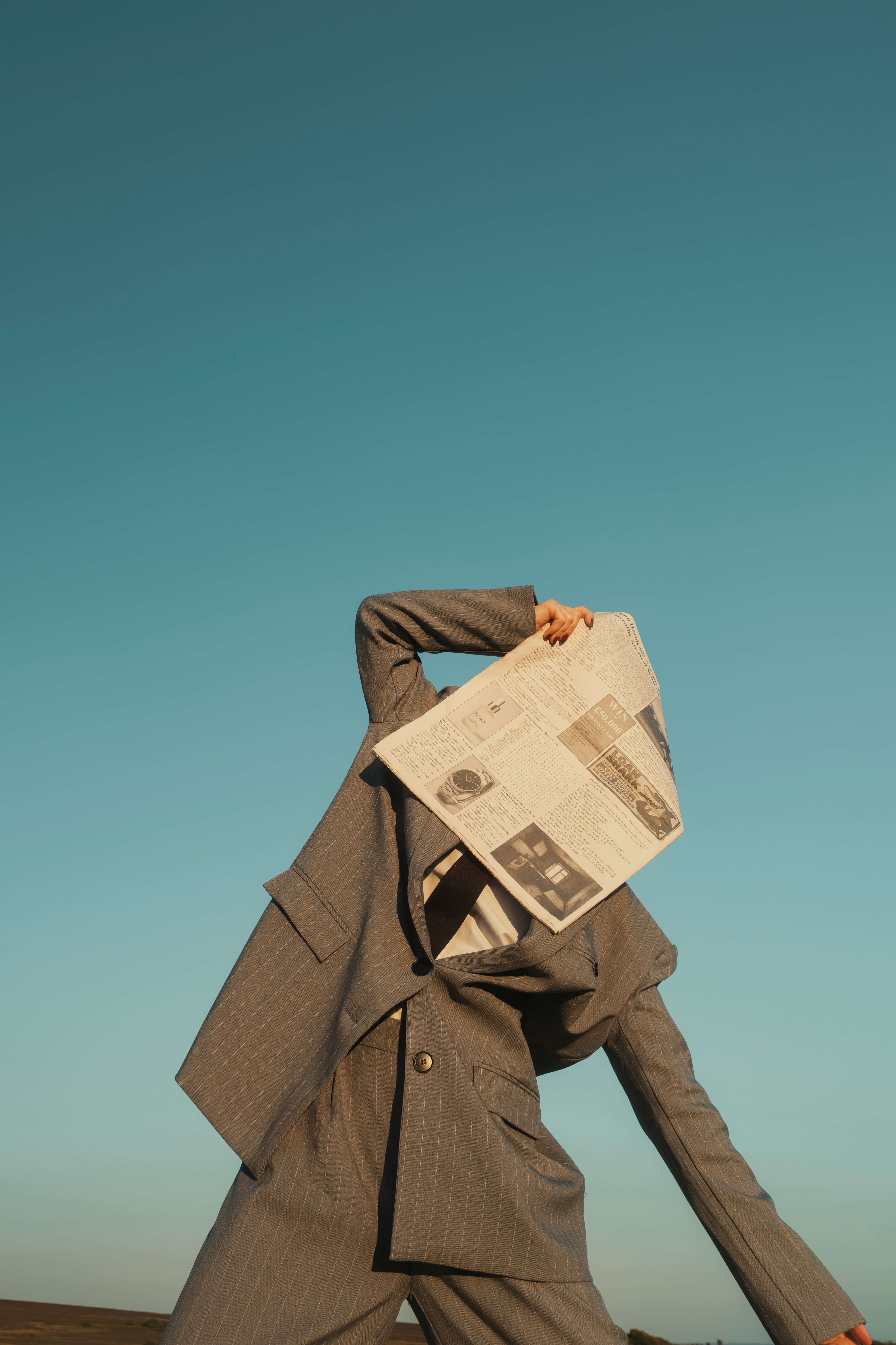 Person in suit holding newspaper over face against sky