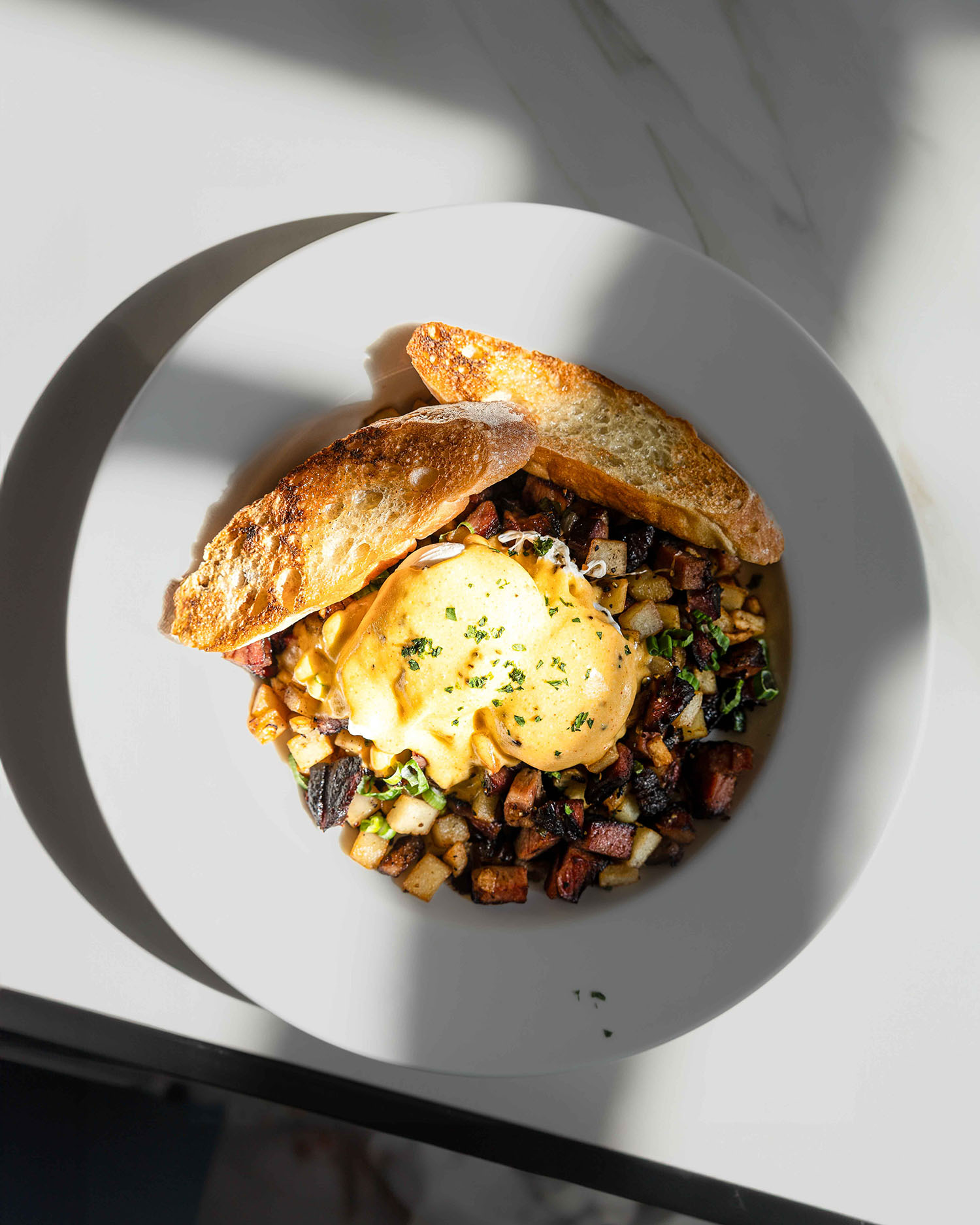 Overhead shot of toast with poached eggs and potatoes with a soft shadow on a marble surface at Hubbard Inn in River North Chicago IL