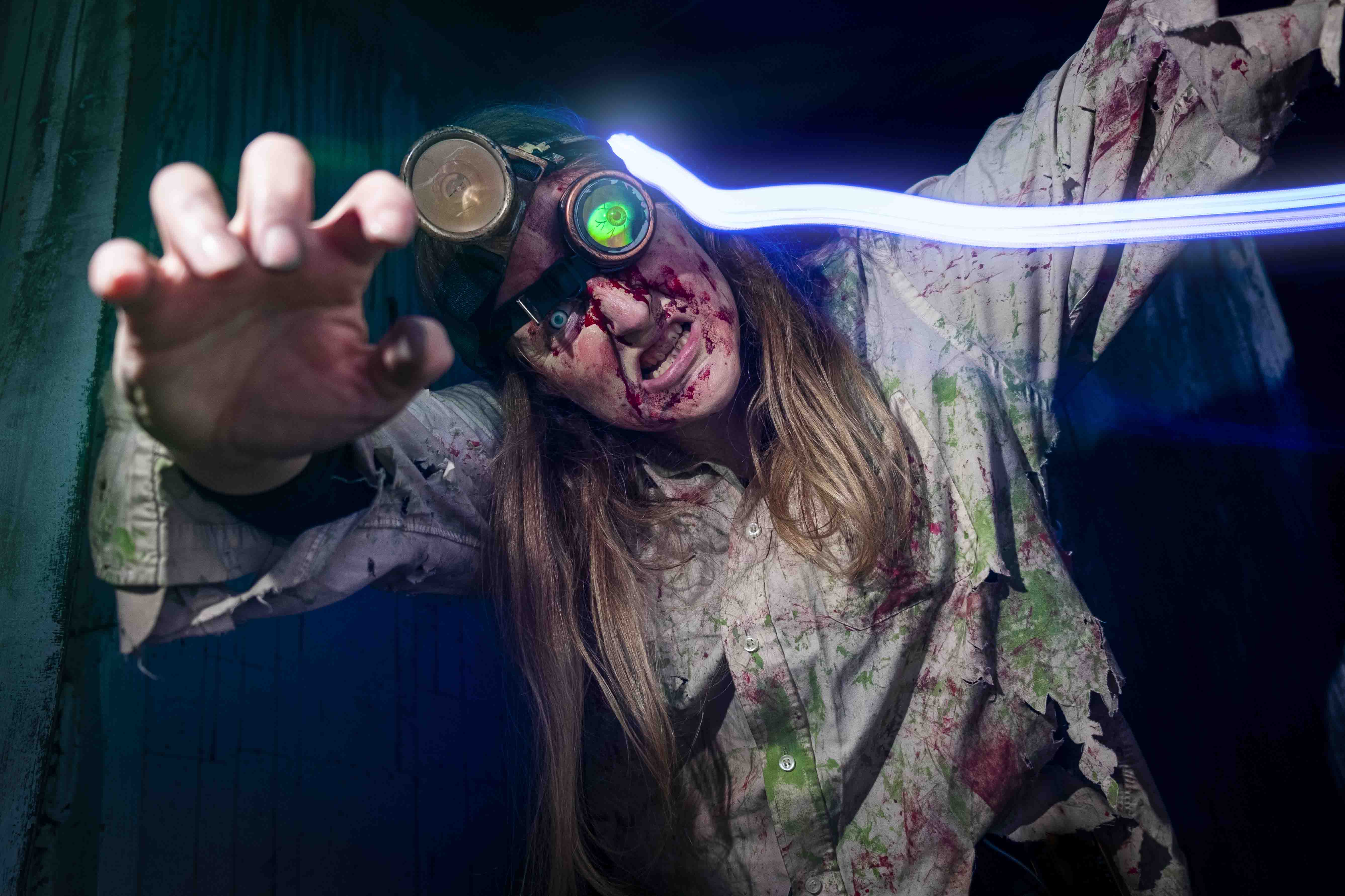 Bloody zombie scientist reaching out with glowing blue light trail behind them.