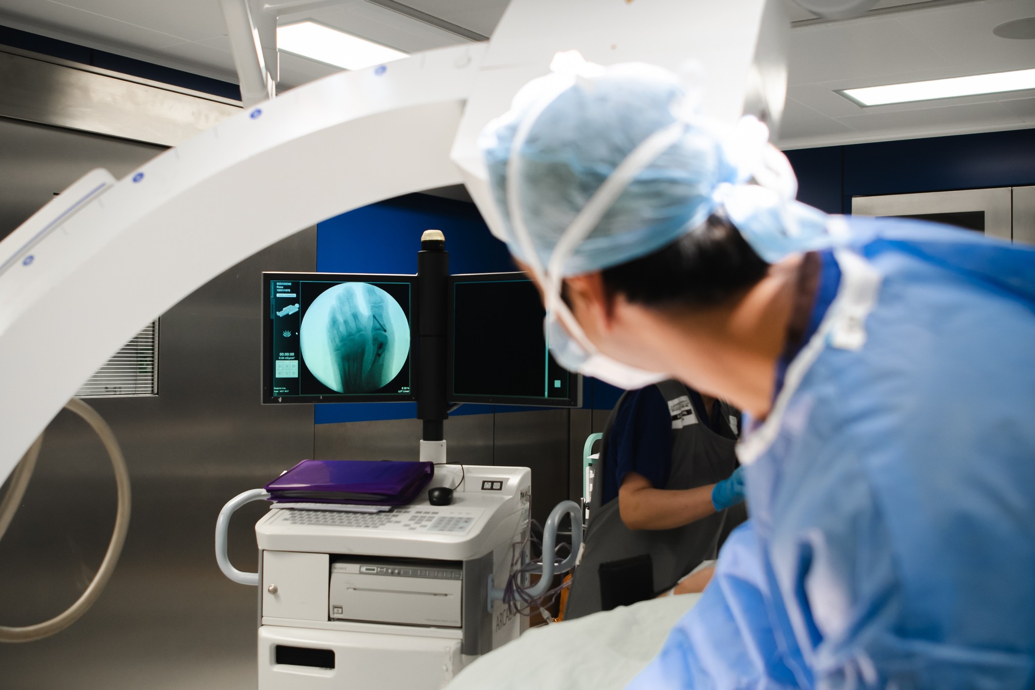 A podiatric surgeon in a theare looking towards an xray screen displaying an image of a foot. 