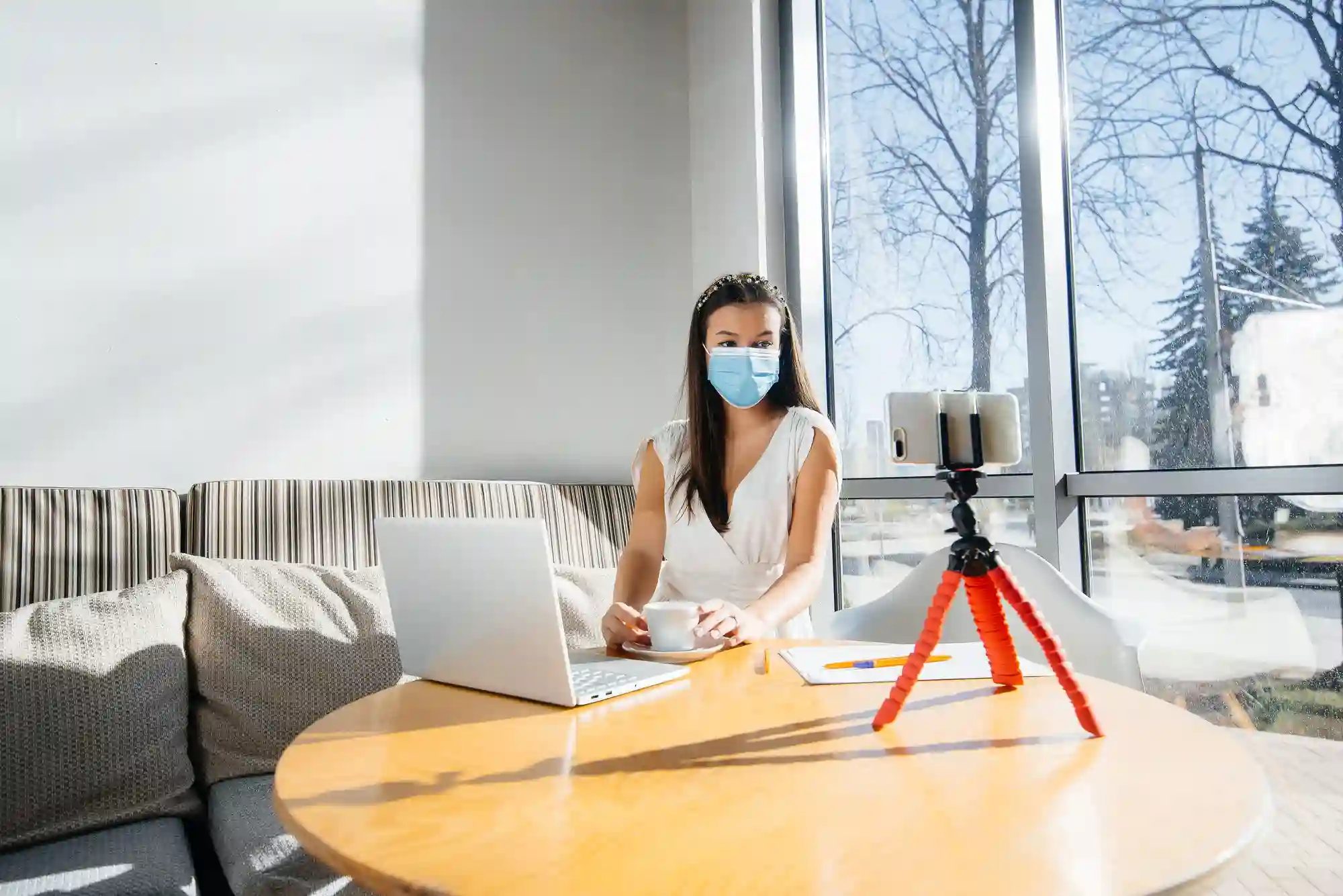 Woman in mask live streams her work on laptop.