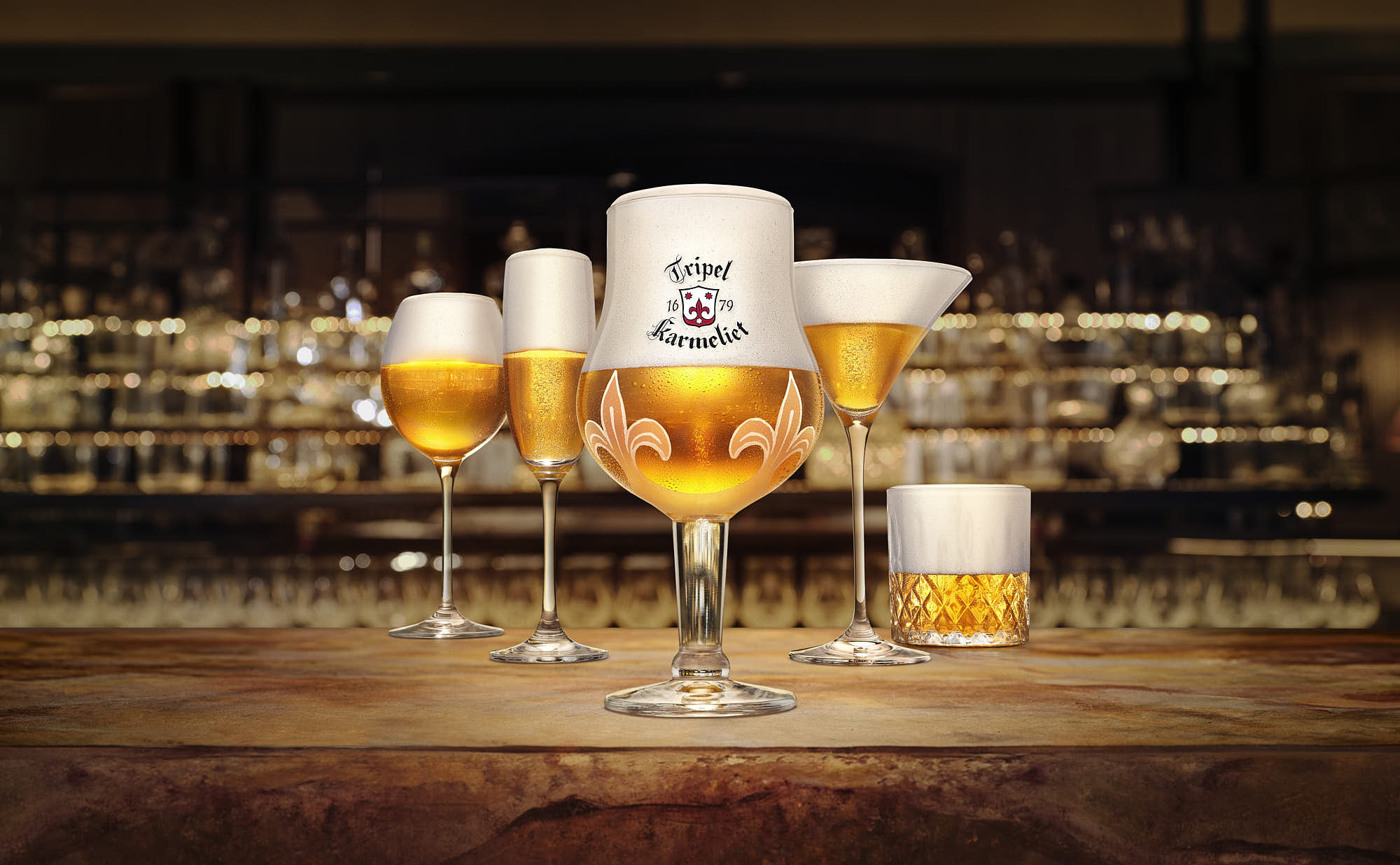 Five glasses of beer are displayed on a bar with a soft glow of lights in the background, creating a warm atmosphere.