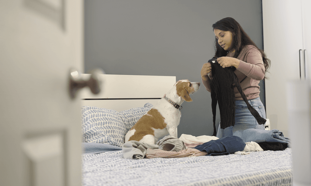 A Woman folding clothes by her bed with a dog on the side