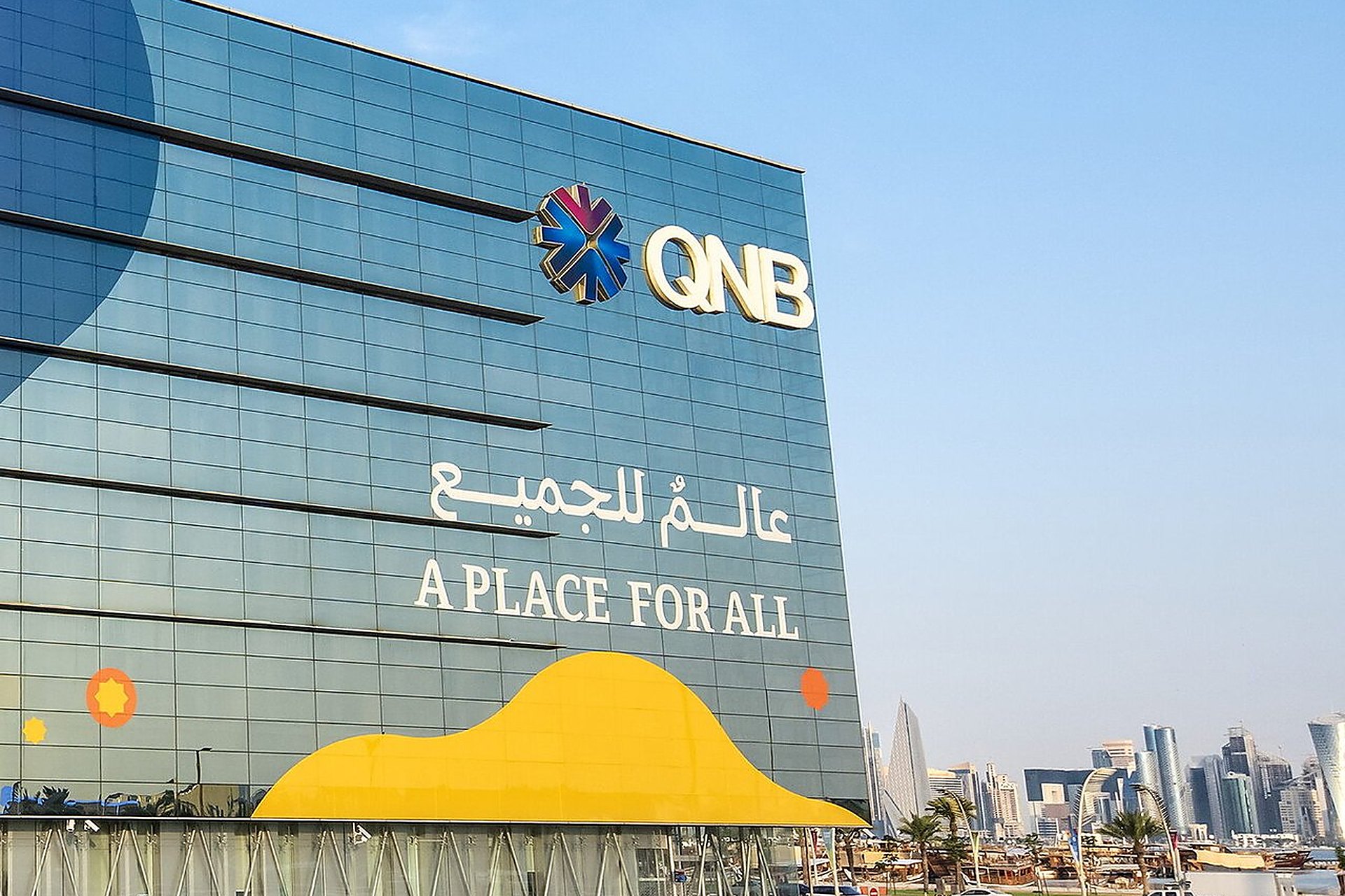 Le siège de la banque QNB, à Doha, sa façade de verre bleu sous un ciel clair, avec les tours de West Bay au loin, l'une des banques qatariennes où ouvrir le compte de sa société