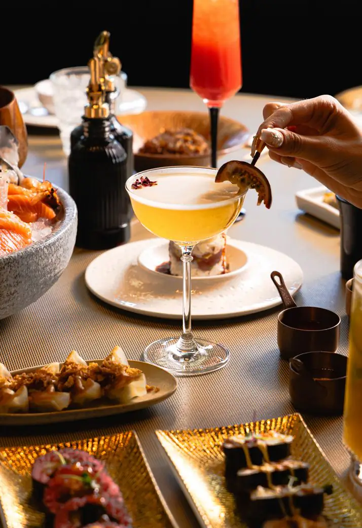 A cocktail served at the table, among sushi and sharing dishes