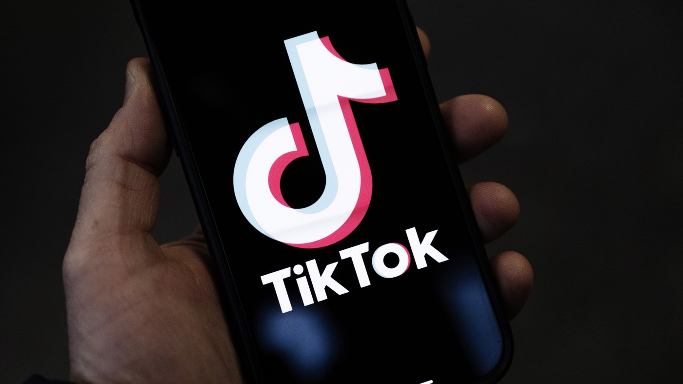  A hand holding a smartphone displaying the TikTok app logo on the screen, with a dark background.