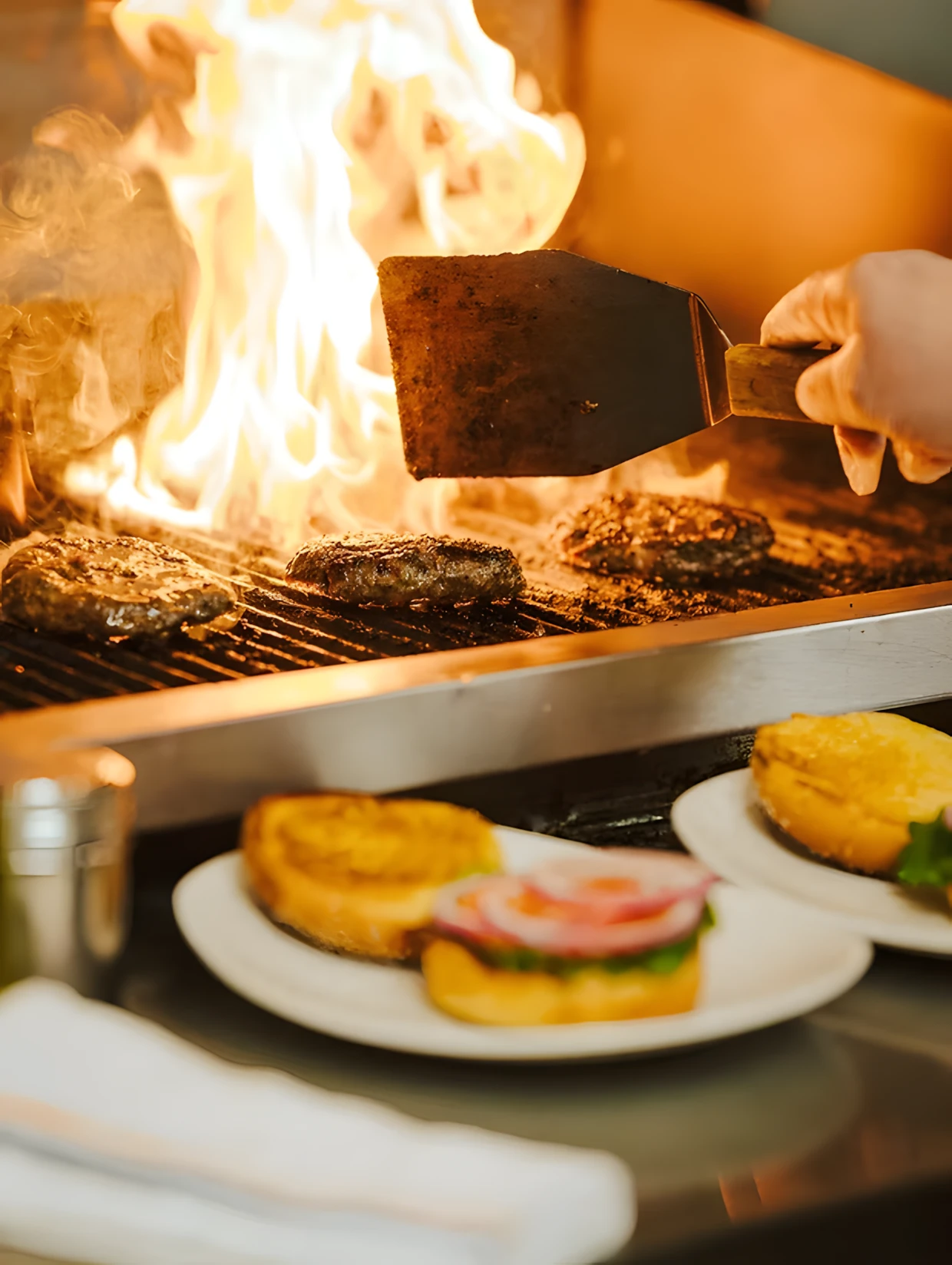 burger buns in fore ground with burgers on the grill in background
