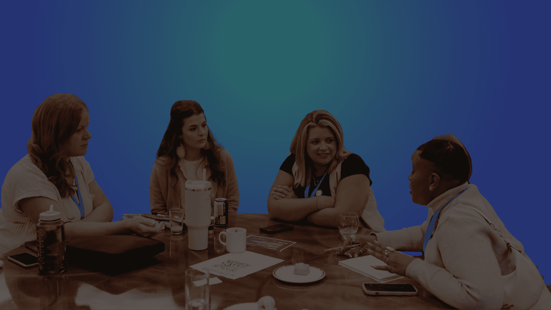 A group of four people engaged in a discussion at a table, with a blue background.