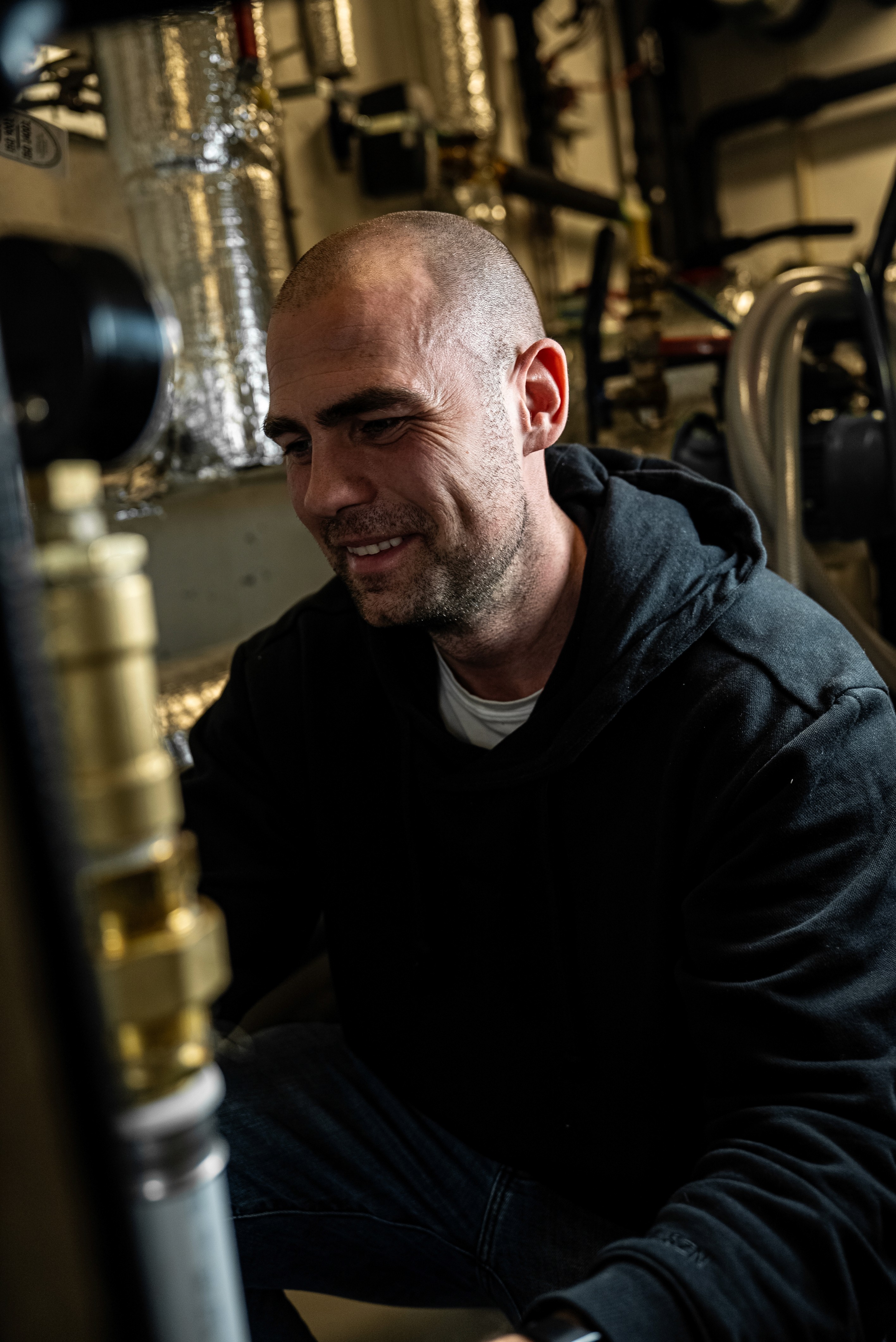 A woman in a mustard yellow top and blue jeans is sitting on a rug, holding a laptop and a small memory card, with a DSLR camera and lens beside her.