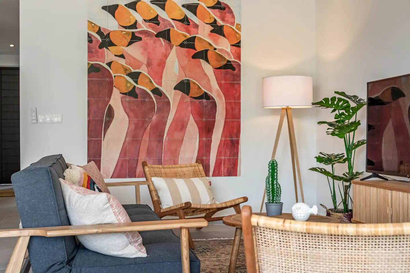 Picture of the interior of the living room of the Breeze Oasis Holiday apartment rental, visible is a wallpaper of flamingo's, a blue couch and a TV