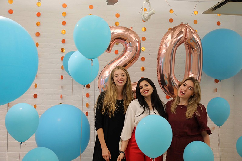A photo of a group of girls surrounded by blue balloons and in the background the number twenty made also from shiny balloons.