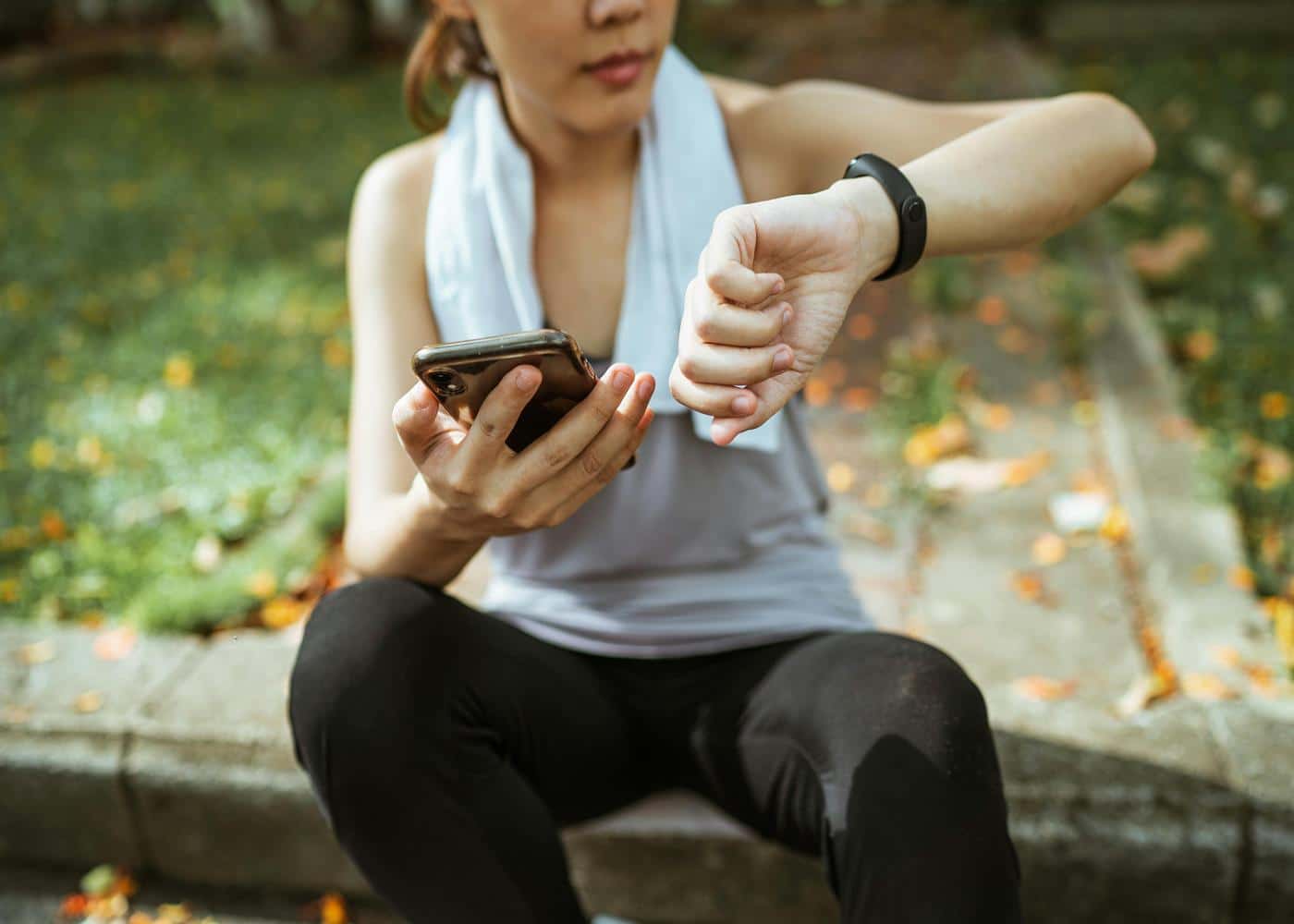 Woman sitting outside looking at smart watch on wrist with phone in other hand