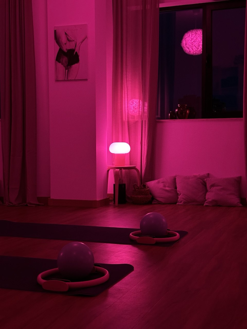 A studio room bathed in vibrant pink and purple mood lighting, featuring Pilates equipment including balls and rings on the floor.
