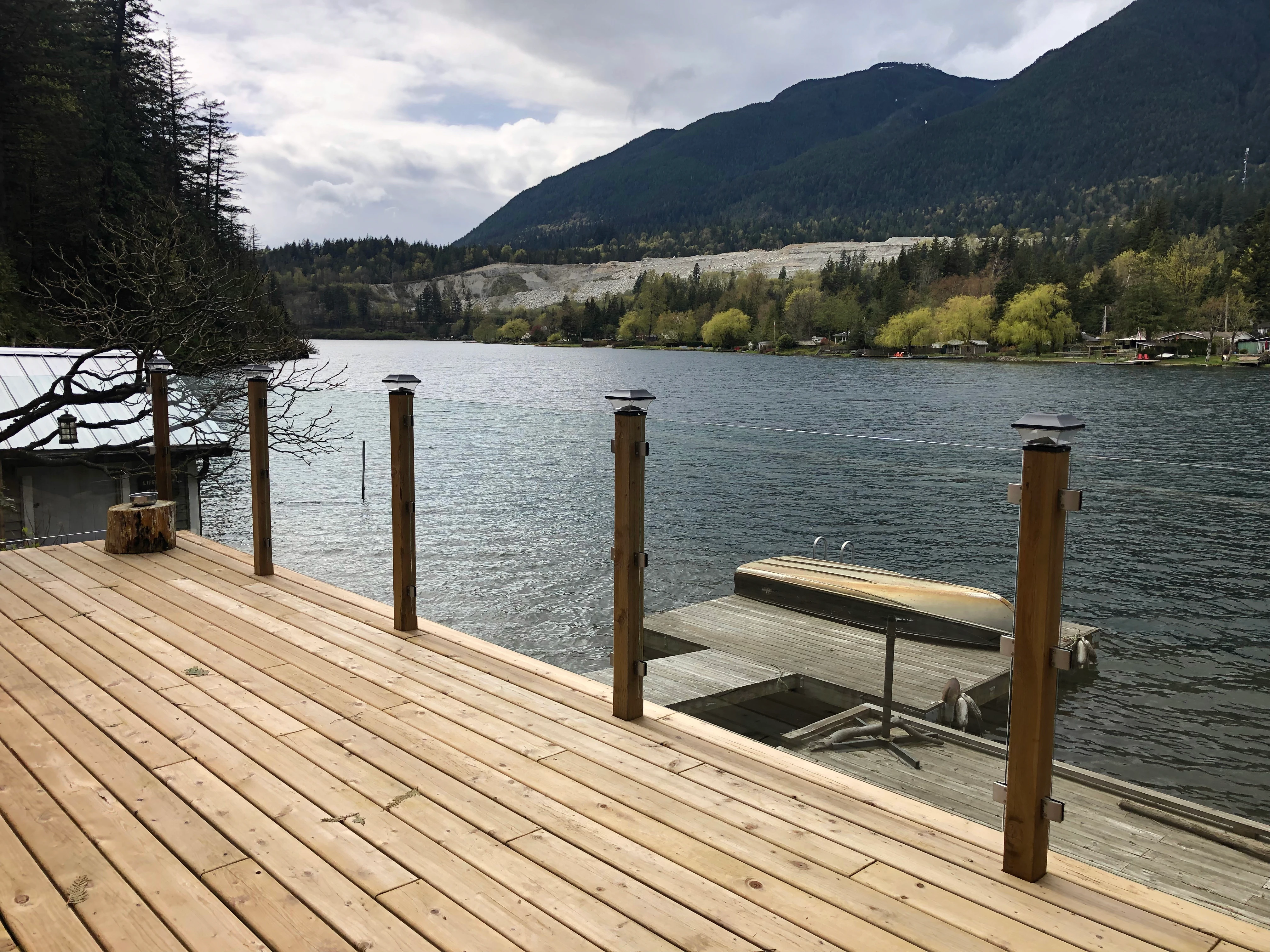 Waterfront deck with glass railing panels mounted between cedar posts, facing open water