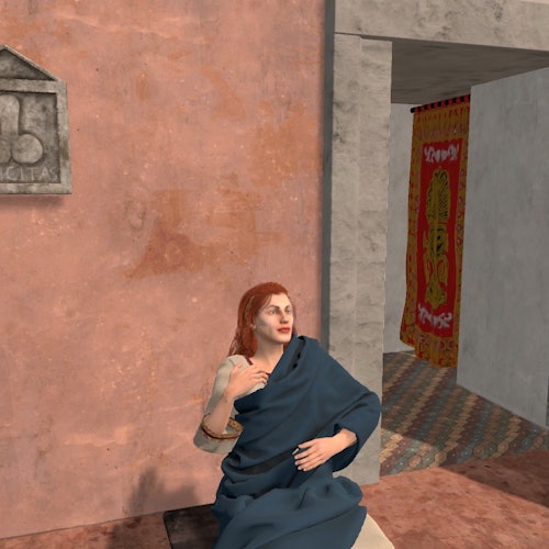 Una persona con lunghi capelli rossi, avvolta in un tessuto blu, seduta contro una parete con texture vicino a una porta con una tenda colorata all'interno.