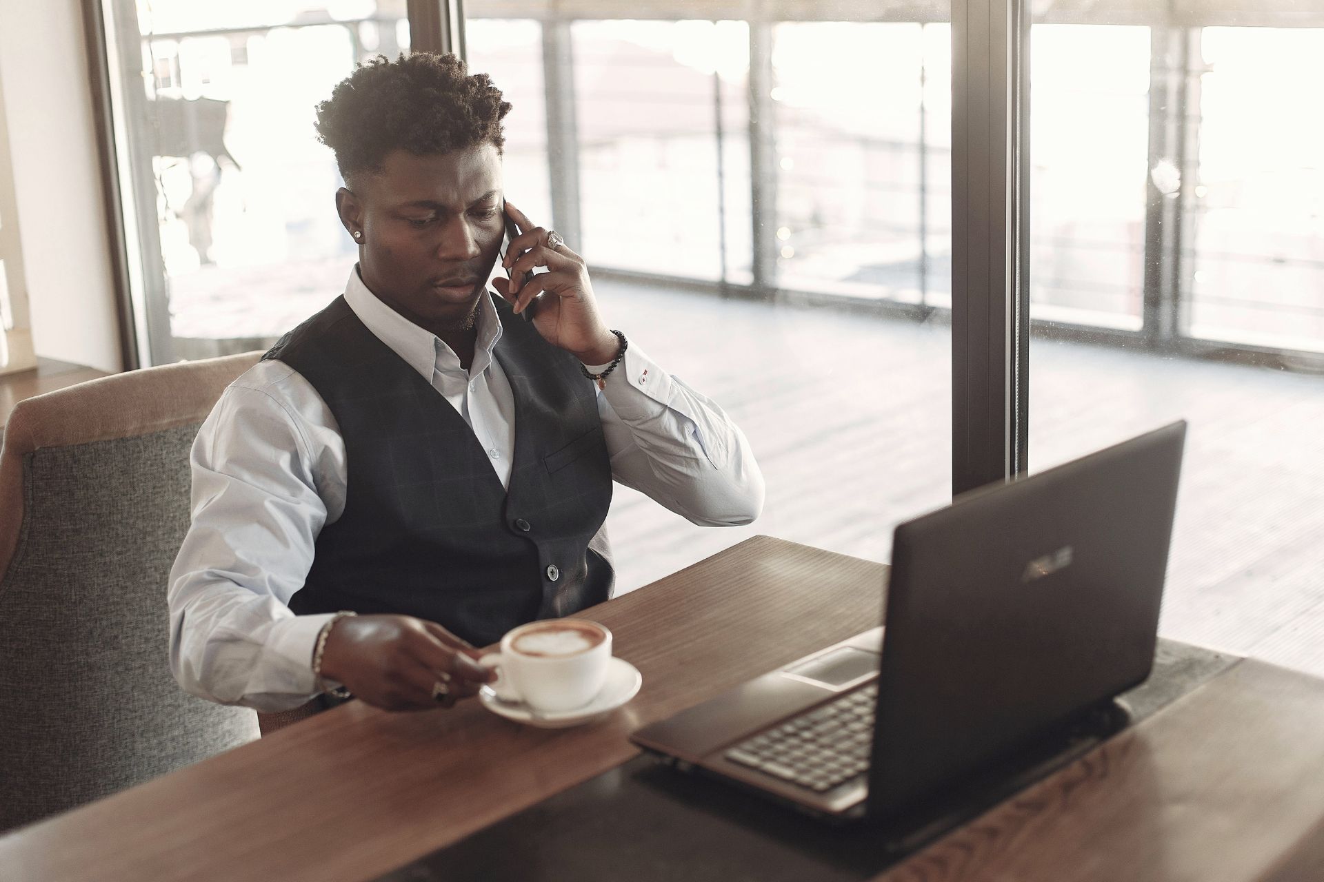 AI automation consultant working on a laptop and taking a business call in a modern office cafe