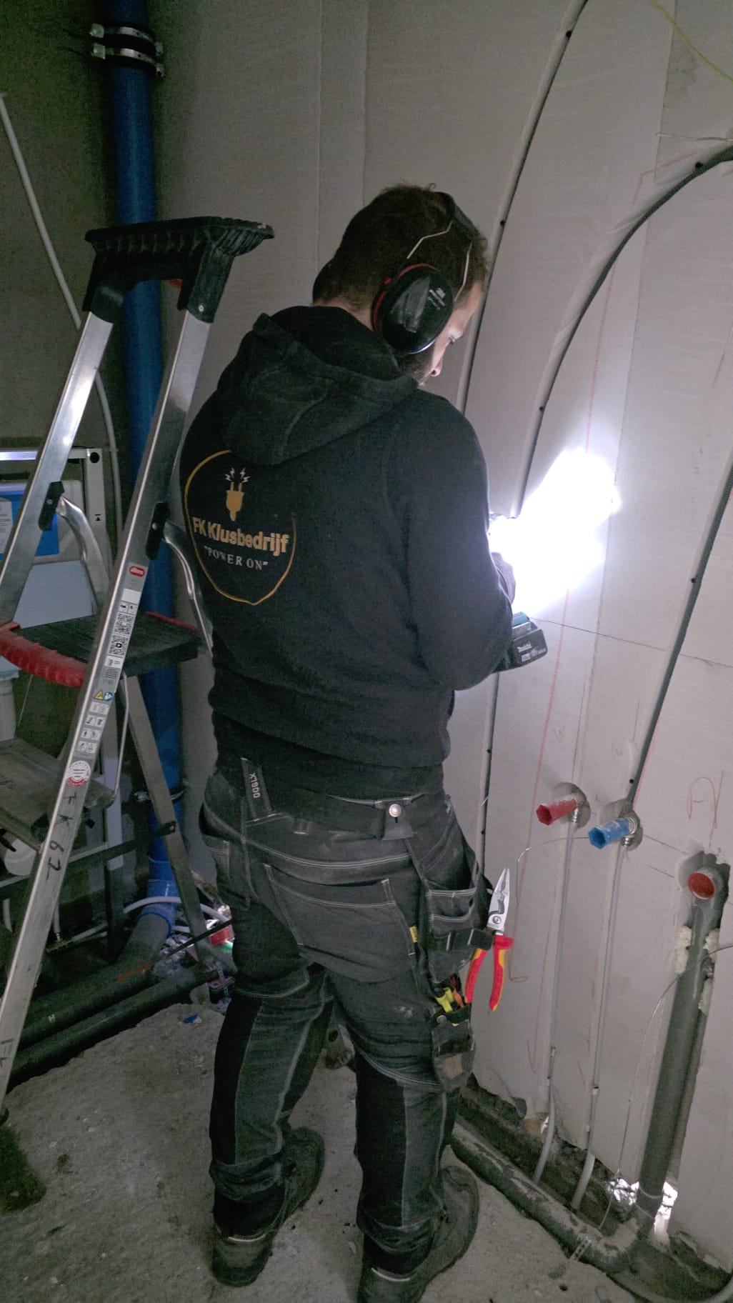 A man wearing glasses and a blazer working at a desk, writing in a notebook beside a computer monitor in a modern office.