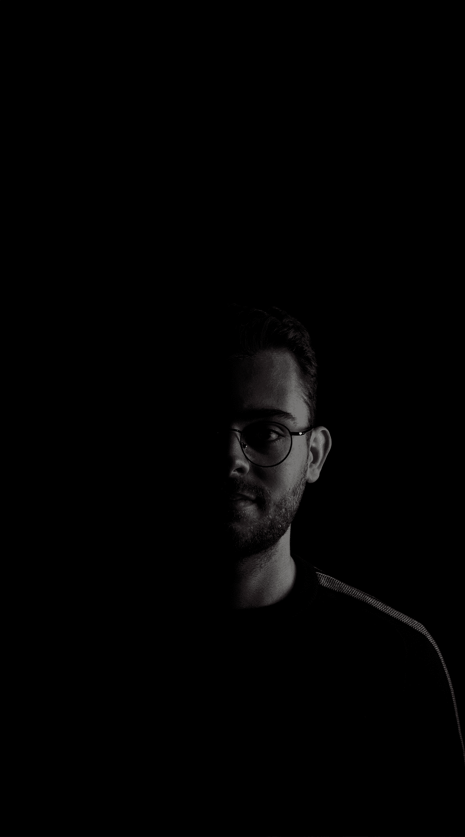 Un homme avec des lunettes, vêtu d'un pull noir.