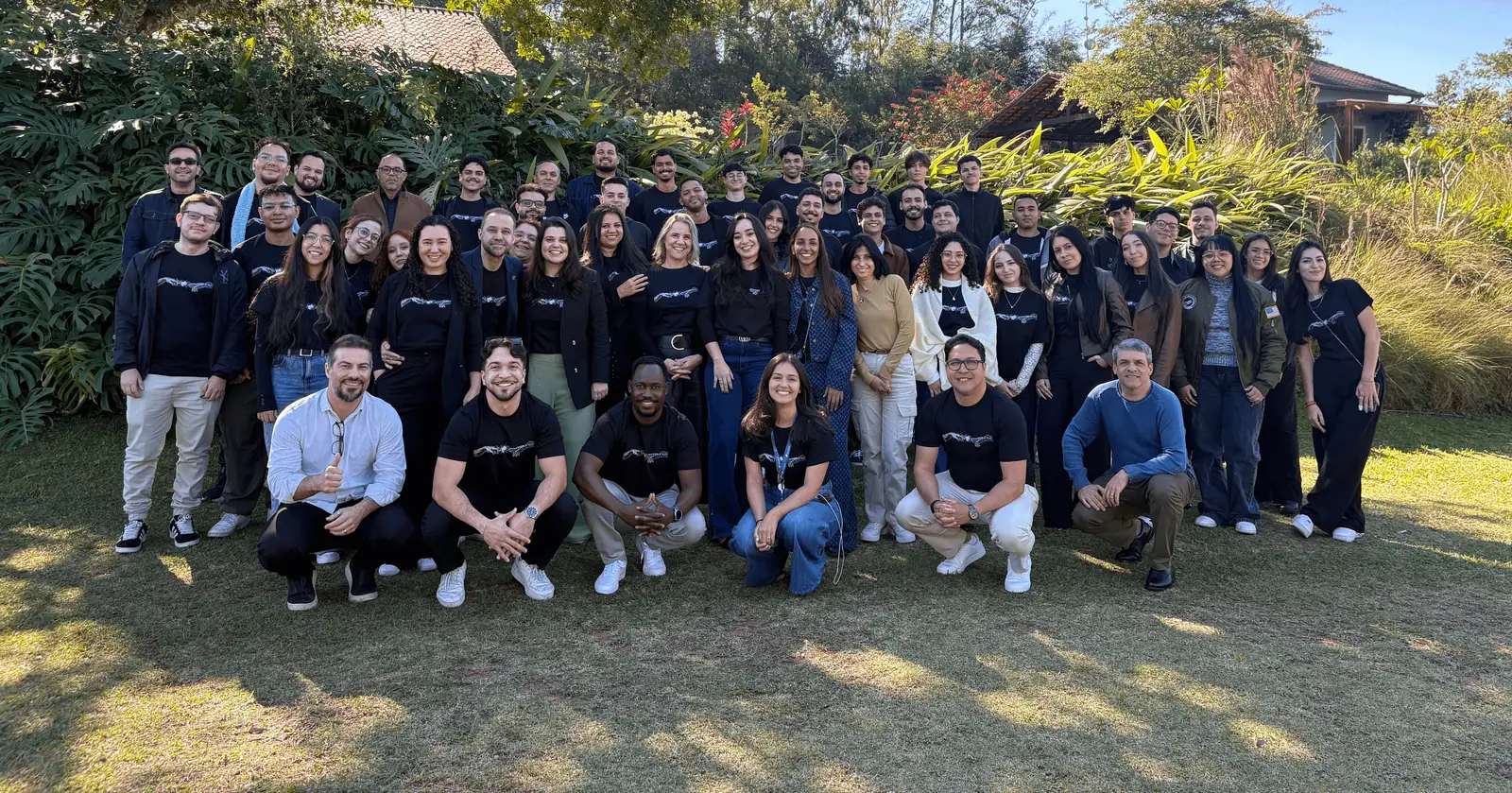 Equipe da Imobzi, sendo um grupo grande de pessoas sorrindo ao ar livre em frente a plantas.