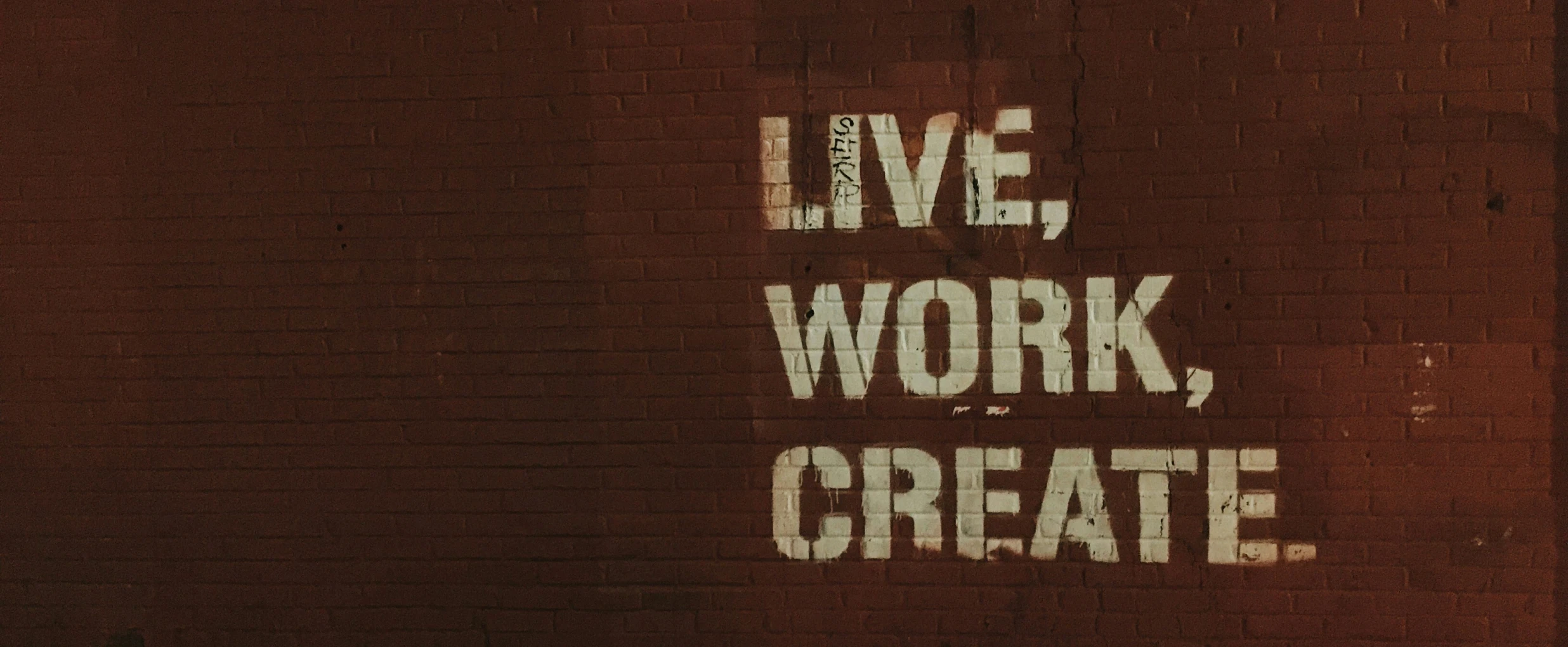 A brick wall with a "live, work, create" message on stencil graffity