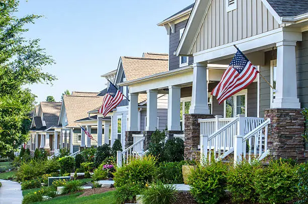 Row of suburban homes decorated with American flags for Labor Day, featuring manicured lawns, front porches, and a clear sunny sky.