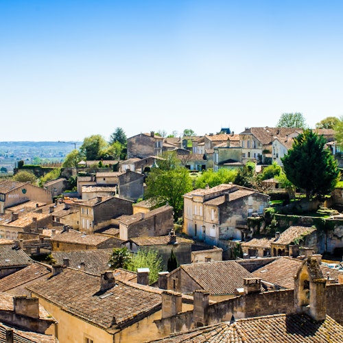 A village with clustered, rustic buildings and tiled roofs, surrounded by greenery under a clear blue sky.