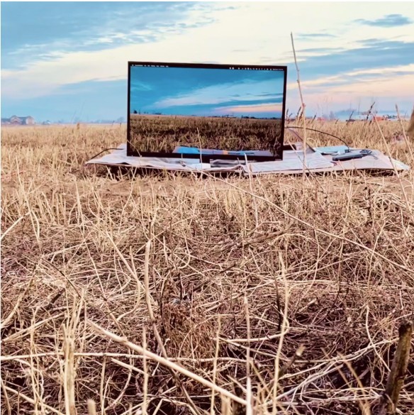 A photo of a field with a TV showing the field and sky