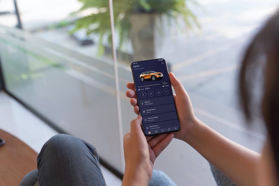 "Técnico de Citroën sonriendo mientras revisa un vehículo blanco con detalles rojos, en un taller con neumáticos al fondo."