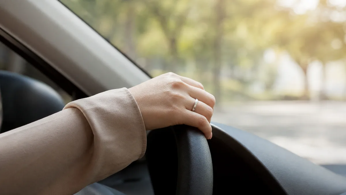 Woman's hand wearing a plain silver dhikr ring on a steering wheel in a parked car