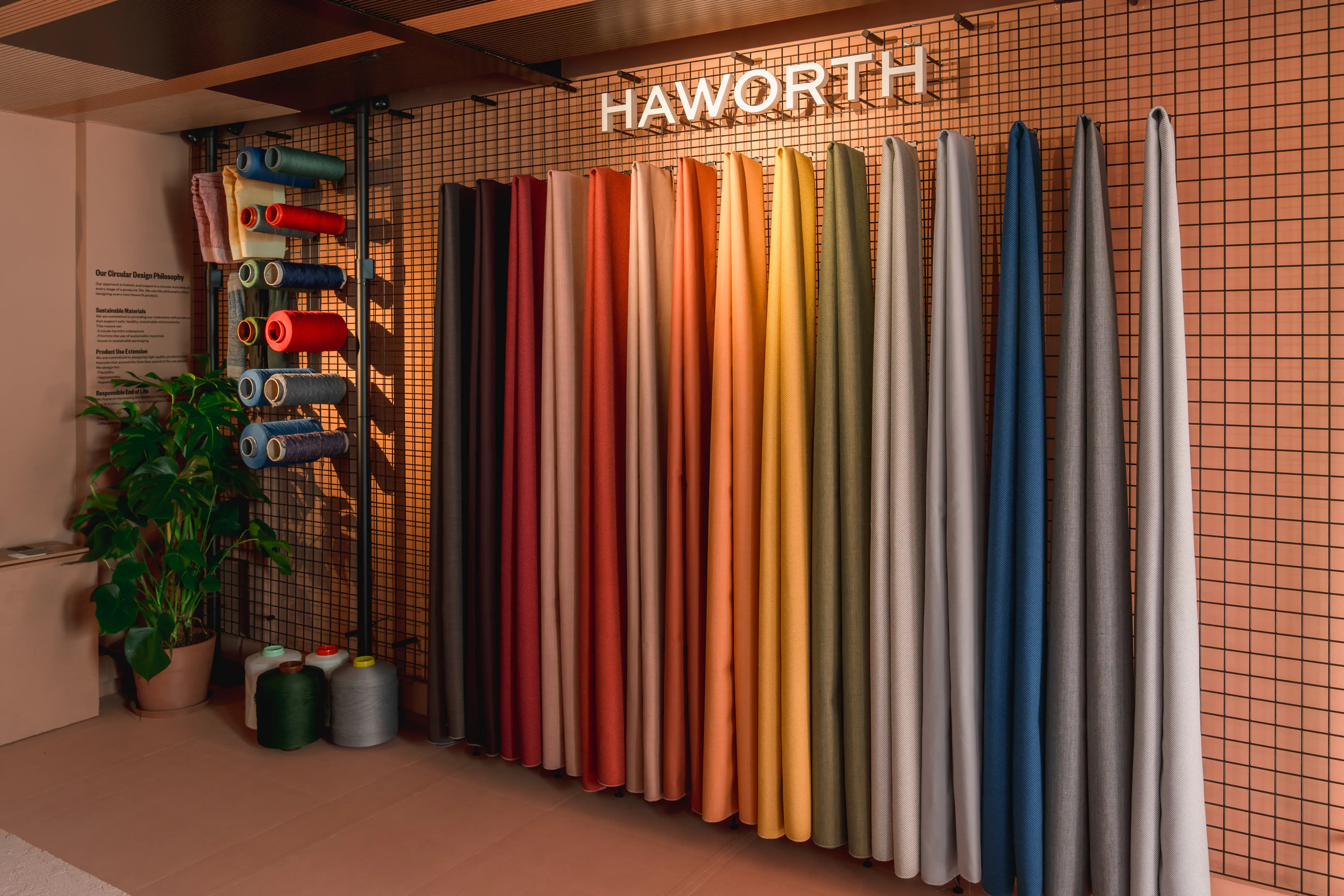 Colorful fabric panels and yarn spools on a grid wall beneath the glowing Haworth logo in the showroom.