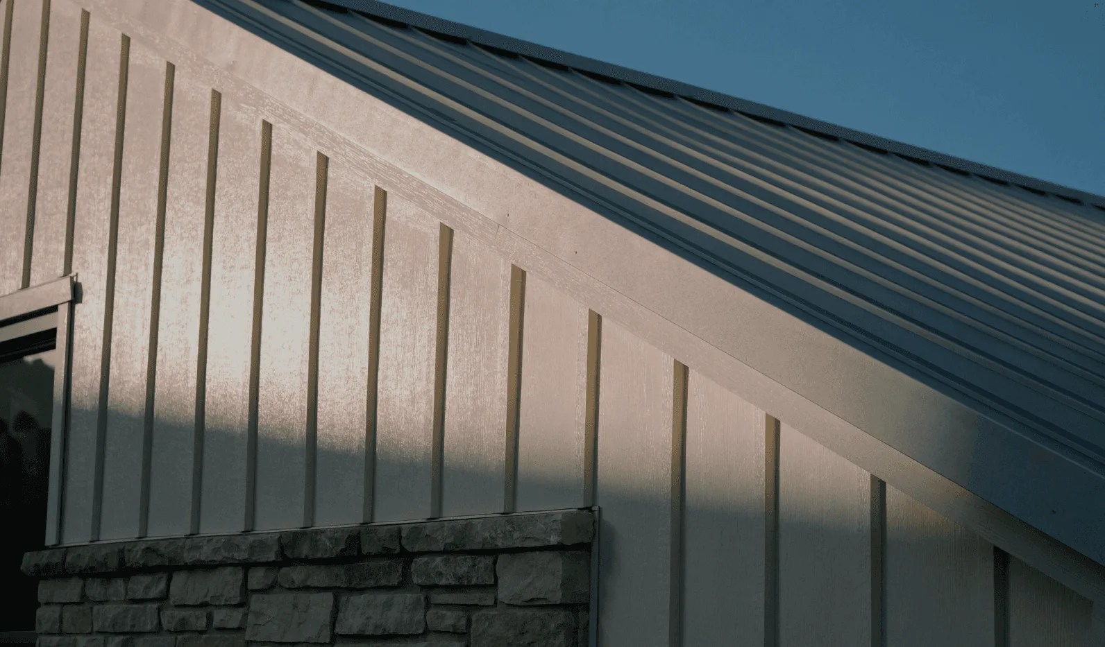 Gable end of a home with vertical board-and-batten siding, metal roof and stone base