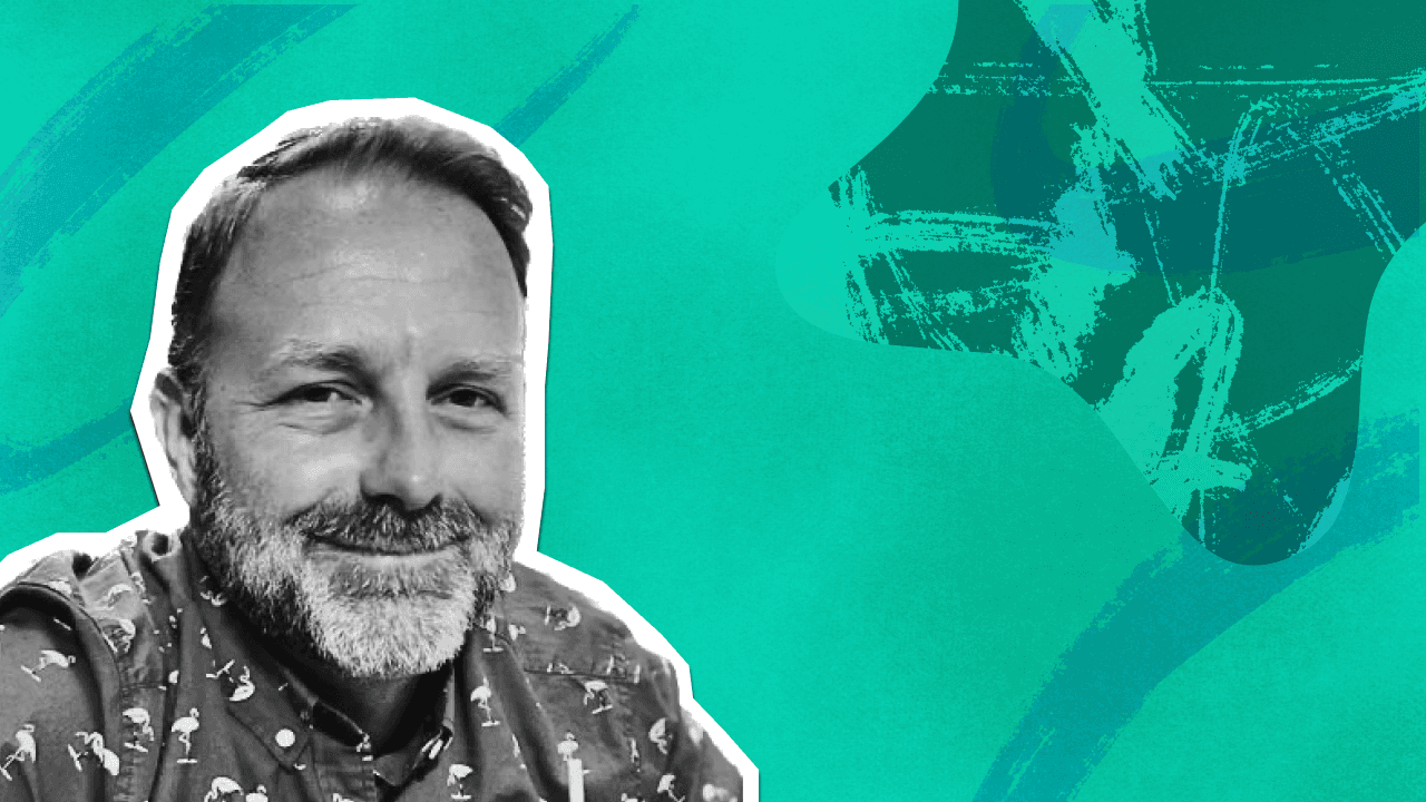 A smiling man with a beard, wearing a flamingo-patterned shirt, against a vibrant abstract background of teal and green.