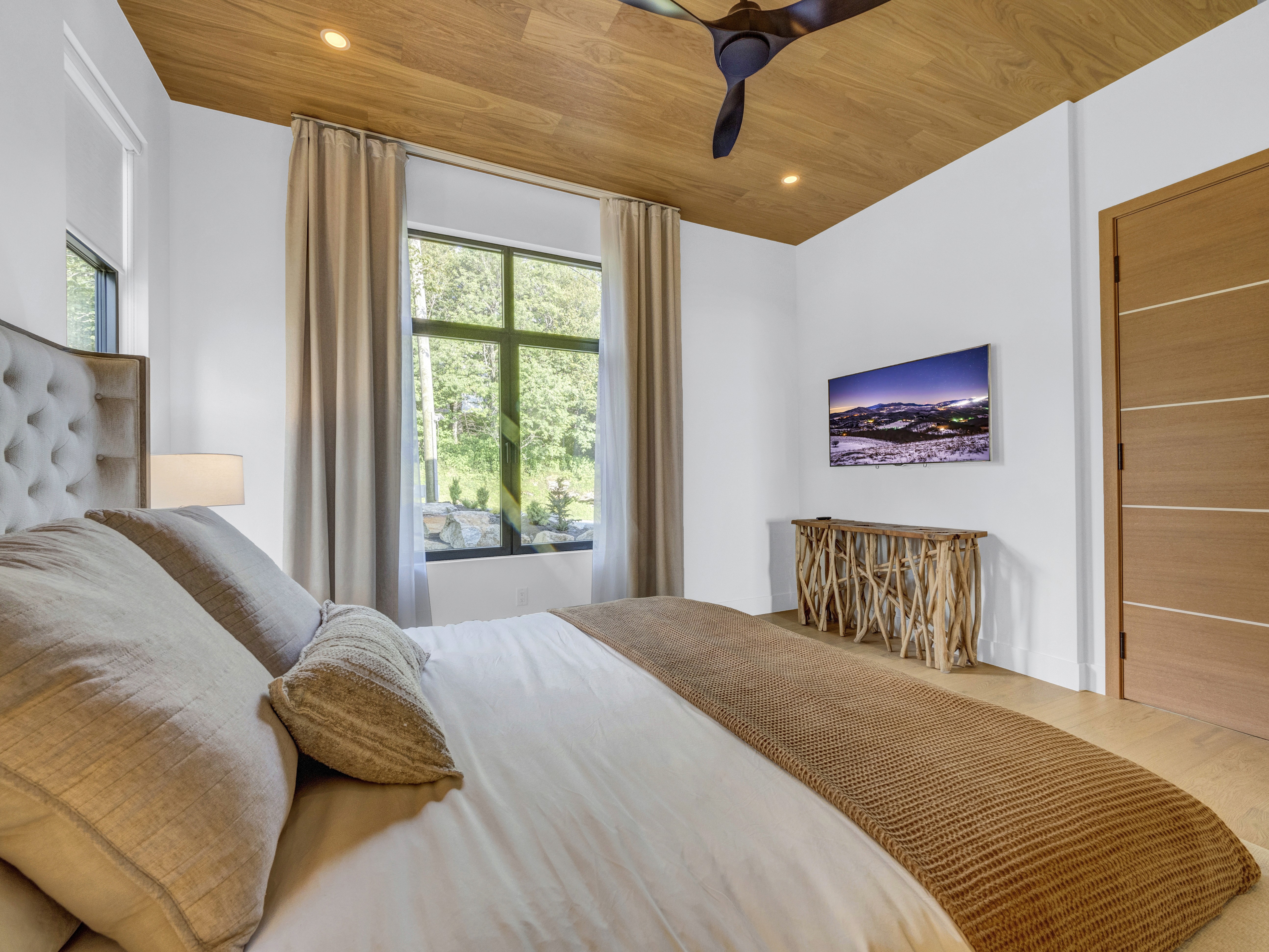 View from the primary bed showing a wall-mounted TV and a unique natural wood console table
